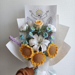 Puede incluir: Un ramo de flores de ganchillo envuelto en papel blanco. El ramo incluye girasoles, lirios, rosas y nomeolvides. Un dibujo de Jes&uacute;s con las palabras "Ha resucitado" es visible en el fondo.