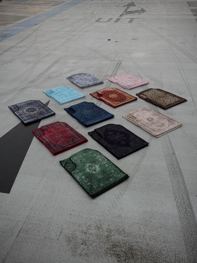 Puede incluir: Una variedad de alfombras de oraci&oacute;n en varios colores, incluyendo azul, rojo, verde y beige, est&aacute;n dispuestas sobre una superficie de hormig&oacute;n. Cada alfombra presenta un dise&ntilde;o ornamental y estampado. La palabra "UIT" es visible en el fondo.