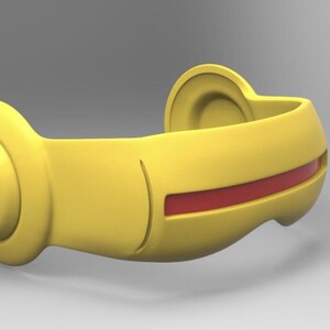 May include: A yellow, curved object with a red stripe. The object has a rounded shape with a circular end on one side and a curved, ear-like shape on the other. The red stripe runs along the center of the object.