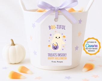 Peut inclure: Un récipient en céramique blanc avec un nœud lilas et une étiquette indiquant "BOO-TIFUL" avec une illustration de fantôme. L'étiquette dit "Treats Inside! Happy Halloween" et "From, Reagan". Des bonbons et une citrouille blanche sont éparpillés.