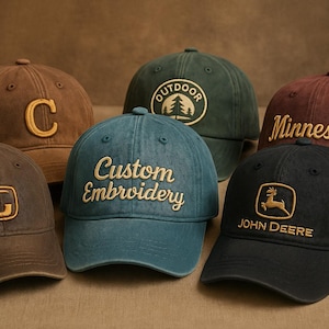 May include: Six baseball caps in various colors, including brown, green, and blue. Each cap features embroidered text or a logo, such as "C", "Outdoor", "Minnesota", "Custom Embroidery", and "John Deere".