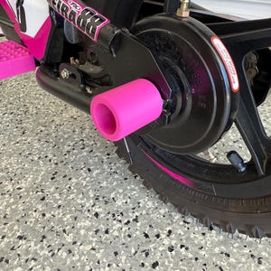 May include: Close-up of a pink bicycle axle peg attached to a black bicycle frame. The bicycle has pink accents and the brand name "Keira & Co" is visible. The tire is black with a pink stripe.