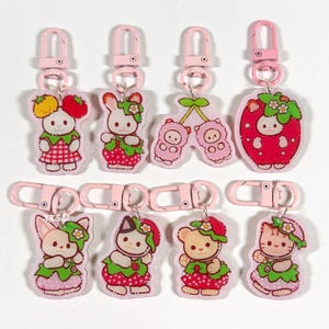 May include: Eight acrylic keychains with pink lobster clasps, featuring various animal characters dressed in fruit-themed outfits, including strawberries, cherries, and flowers. Each charm displays a unique character design with vibrant red, pink, and green colors.