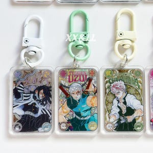 K&ouml;nnte beinhalten: Acryl-Schl&uuml;sselanh&auml;nger mit farbenfrohen Illustrationen von Anime-Charakteren. Jeder Schl&uuml;sselanh&auml;nger hat einen Metallverschluss in Wei&szlig;, Gr&uuml;n oder Creme. Die Schl&uuml;sselanh&auml;nger zeigen die Namen der Charaktere und sind rechteckig.