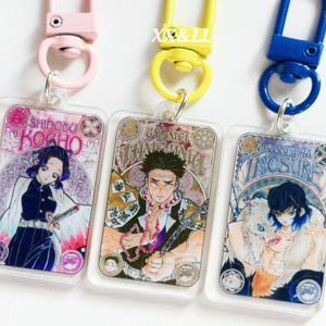 K&ouml;nnte beinhalten: Drei Schl&uuml;sselanh&auml;nger aus Acryl mit farbenfrohen Illustrationen von Anime-Charakteren. Jeder Schl&uuml;sselanh&auml;nger hat ein anderes Charakterdesign und einen farblich passenden Verschluss in Rosa, Gelb und Blau. Die Schl&uuml;sselanh&auml;nger zeigen japanischen Text und dekorative Bord&uuml;ren.