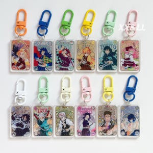 K&ouml;nnte beinhalten: Sammlung von Anime-Schl&uuml;sselanh&auml;ngern mit farbenfrohen Metallverschl&uuml;ssen. Jeder Schl&uuml;sselanh&auml;nger zeigt eine Charakterillustration in einem rechteckigen, transparenten Acrylrahmen. Die Verschl&uuml;sse sind in verschiedenen Farben erh&auml;ltlich, darunter Orange, Blau, Gr&uuml;n, Gelb und Rosa.