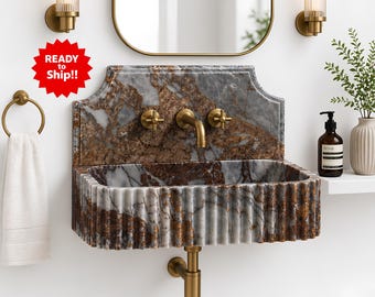 May include: A wall-mounted marble sink with a fluted basin and a patterned backsplash. The sink has brass fixtures, including a faucet and cross-handle valves. A white towel hangs on a brass ring, and a mirror is above the sink.