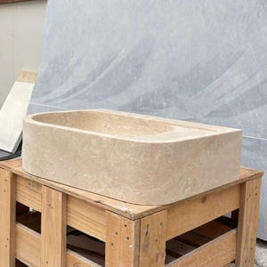 Travertine marble sink displayed on wooden crate in workshop area