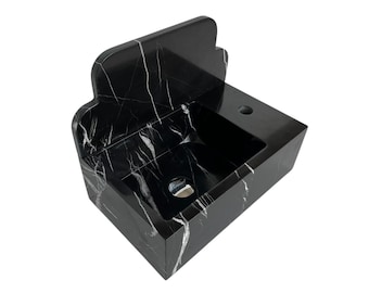 May include: A black marble sink with white veining. The sink has a rectangular basin and a back splash with a decorative top edge. A faucet hole is visible on the right side of the sink.