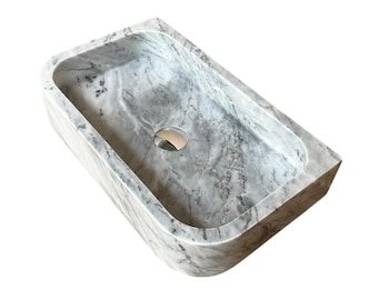 May include: Rectangular marble sink with rounded corners. The sink is gray with white veining and a circular drain. The design is modern and minimalist, suitable for a bathroom.