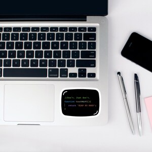 May include: A black sticker with a white border, displaying computer code and the text "//Don't. Just don't. function touchMyPC(){ return 'SLAP SO HARD'; }", is placed on a laptop. A smartphone and two pens are also visible.