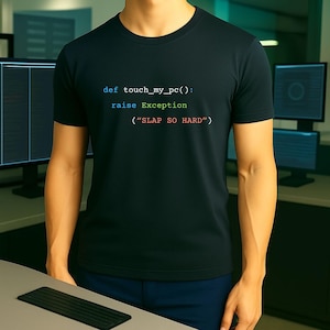 May include: Black crew neck t-shirt with the text "def touch_my_pc(): raise Exception ("SLAP SO HARD")" in a colorful, code-like font. The shirt is worn by a person in a tech-related environment.