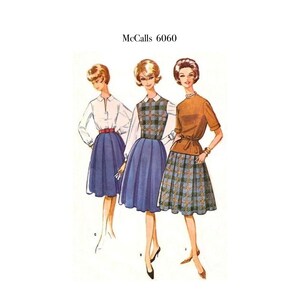 May include: A vintage sewing pattern envelope labeled McCalls 6060 featuring illustrations of three outfits. The designs include a white blouse with a blue pleated skirt, a plaid bodice with a blue skirt, and a brown top with a plaid skirt.