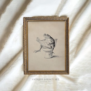 May include: A framed vintage print depicting a frog reading a newspaper while seated on a toilet. The artwork is in monochrome, with the frog and toilet intricately drawn. The frame is gold-coloured with decorative detailing. The text "ANTIQUE LEGACY ART" is at the bottom.