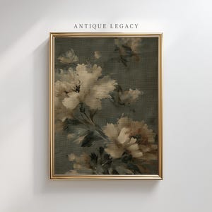 Op de afbeelding: Een ingelijste bloemenprint met een gouden lijst. Het kunstwerk toont grote, cr&egrave;mewitte bloemen tegen een donkergroene achtergrond. De woorden "ANTIQUE LEGACY" staan bovenaan het frame.