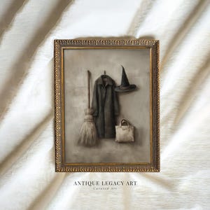 May include: Framed artwork depicting a witch-themed still life. A dark coat hangs on a hook beside a witch's hat and a beige tote bag. A broom leans against the wall. The frame is gold with ornate detailing. Text at the bottom reads "ANTIQUE LEGACY ART Curated Art."
