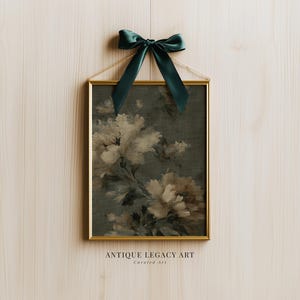 Op de afbeelding: Een ingelijste bloemenprint met een gouden lijst en een donkergroene strik aan de bovenkant. Het kunstwerk toont grote, lichtgekleurde bloemen tegen een donkergroene achtergrond. De tekst "ANTIQUE LEGACY ART" en "Curated art" is onderaan zichtbaar.