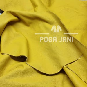 May include: Close-up of a piece of bright yellow leather. The leather is folded and textured, with visible grain and slight imperfections. The text "POGA JANI" is printed in white, with a logo above the text.