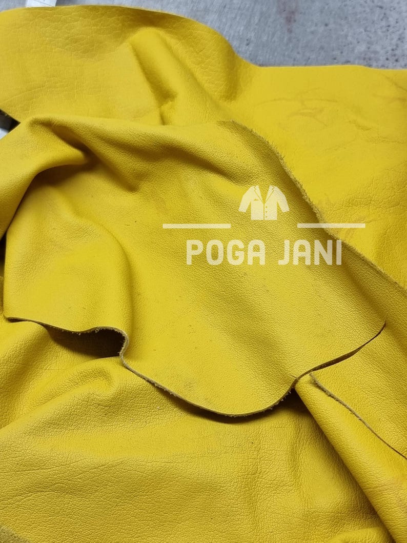 May include: Close-up of a piece of bright yellow leather. The leather is folded and textured, with visible grain and slight imperfections. The text "POGA JANI" is printed in white, with a logo above the text.