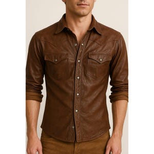 May include: A brown leather shirt with a classic Western design. The shirt features two chest pockets, snap closures, and a collared neckline. The long sleeves are cuffed at the wrists. The shirt is made of a rich, textured leather.