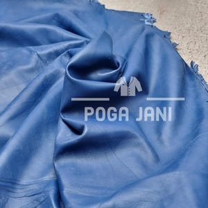 May include: A piece of deep blue leather with visible folds and a textured surface. The text "POGA JANI" is visible in white. A yellow measuring tape is in the background.