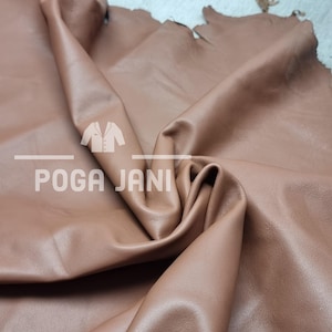 May include: A close-up of a large piece of brown leather with a soft, supple texture. The leather is folded, revealing its thickness and natural grain. The text "POGA JANI" is printed on the leather.