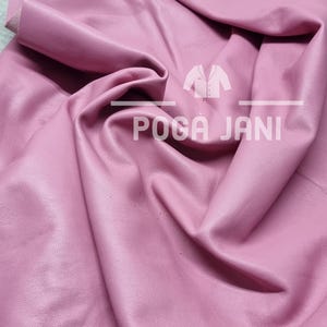 May include: A sheet of pink leather with a textured surface. The leather is folded and draped, showing its flexibility. The text "POGA JANI" is visible on the leather.
