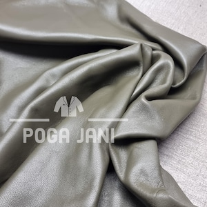 May include: Olive green leather fabric with visible folds and a soft sheen. The fabric is draped, showcasing its texture and flexibility. The text "POGA JANI" is printed on the fabric.