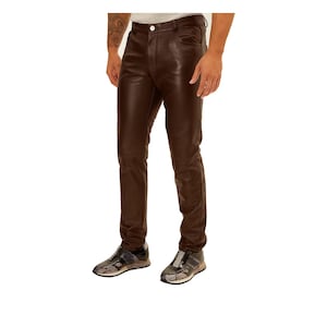 May include: Brown leather trousers with a button closure and belt loops. The trousers have a classic five-pocket design and a slim fit. The model is wearing trainers.
