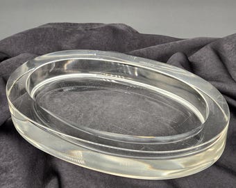 Op de afbeelding: Doorzichtig, ovaalvormig glazen schaaltje met een opstaande rand. Het schaaltje heeft een glad, transparant uiterlijk en is waarschijnlijk bedoeld voor decoratieve doeleinden of als serveerschaal. Het ontwerp is eenvoudig en elegant, geschikt voor diverse interieurstijlen. Ongeveer 20 cm lang.