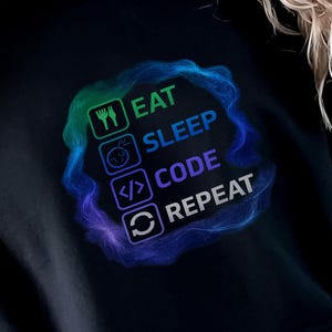 May include: Black hoodie with the text "EAT SLEEP CODE REPEAT" in a colorful, circular design. The design includes icons representing eating, sleeping, coding, and repeating. The hoodie is a comfortable, casual garment.