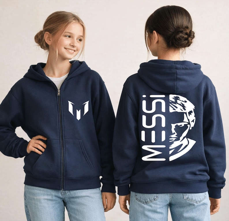 Puede incluir: Una sudadera con capucha y cremallera azul marino que presenta un logotipo blanco en el pecho izquierdo y un gr&aacute;fico grande en blanco en la espalda. El dise&ntilde;o trasero muestra el texto MESSI verticalmente junto a un retrato estilizado.