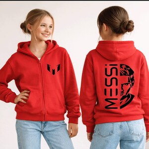 Puede incluir: Una sudadera con capucha y cremallera de color rojo brillante con un logotipo negro en el pecho izquierdo. La parte posterior muestra el texto MESSI verticalmente junto a una ilustraci&oacute;n gr&aacute;fica negra de un rostro. Incluye capucha, mangas largas y dos bolsillos.
