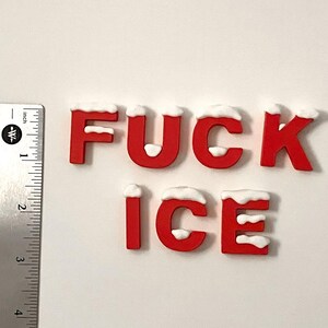 Pu&ograve; includere: Lettere rosse che compongono la scritta "FUCK ICE" con accenti bianchi simili alla neve sulla parte superiore. Un righello di metallo con misure in pollici si trova sul lato sinistro dell'immagine. Le lettere sono alte circa 2,5 cm.