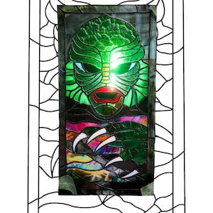 May include: A stained glass window depicting the Creature from the Black Lagoon. The window is framed in black and features a green, black, and purple color scheme. The text "Mama Voodoo Art" is at the bottom of the image.