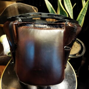 May include: A brown leather boxing headguard with black straps and a padded interior. The headguard is designed to protect the head and face during boxing training.
