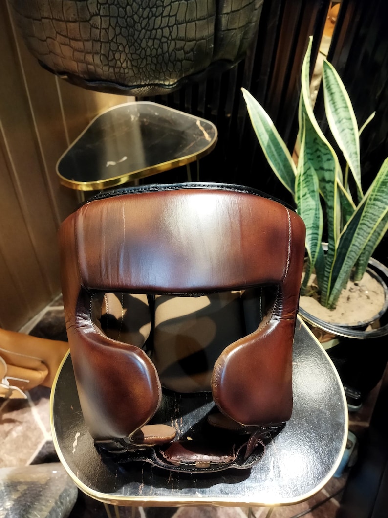 May include: A brown leather boxing headgear with padding around the ears and forehead. The headgear is designed to protect the head during boxing training.
