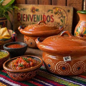 May include: A collection of terracotta serving dishes and bowls, filled with salsa, guacamole, and tortilla chips. The dishes are decorated with white dotted patterns. A wooden sign with the word "Bienvenidos" is in the background.