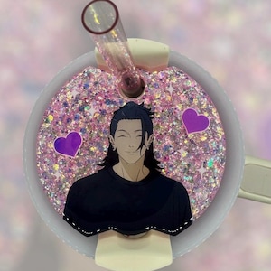 May include: A pink glitter tumbler lid with a cartoon illustration of a smiling character in a black shirt. The lid has a clear straw and two purple heart accents.