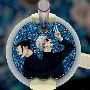May include: A round, white and blue glitter resin pendant featuring two anime characters. One character has white hair and sunglasses, making a peace sign. The other has black hair. A clear straw is attached.