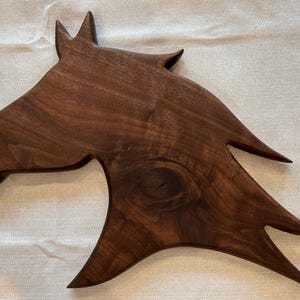 May include: A wooden horse head sculpture, crafted from dark brown wood. The sculpture features a detailed horse head with pointed ears and a flowing mane. The wood grain is visible. Ideal for home decor, this piece measures approximately 76 cm in length.