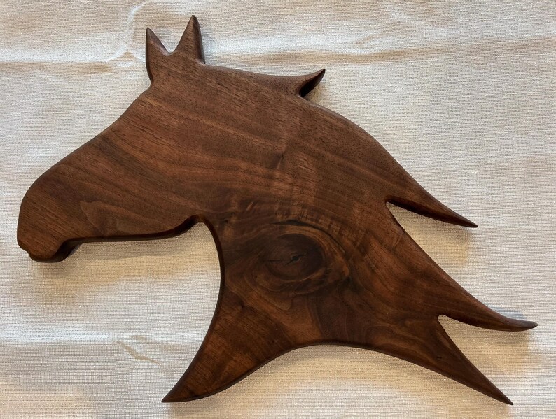May include: A wooden horse head sculpture, crafted from dark brown wood. The sculpture features a detailed horse head with pointed ears and a flowing mane. The wood grain is visible. Ideal for home decor, this piece measures approximately 76 cm in length.