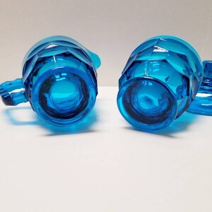 May include: A vintage blue glass creamer and sugar bowl set with a faceted design. The creamer has a handle and the sugar bowl has a lid.