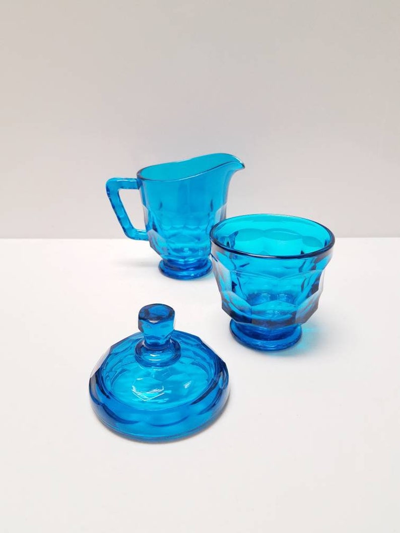May include: A blue glass sugar bowl with a lid and a matching creamer. The sugar bowl and creamer have a faceted design.