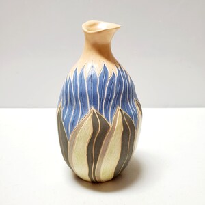 May include: A ceramic vase with a light brown glaze and a blue, green, and brown abstract design. The vase has a narrow neck and a rounded body.