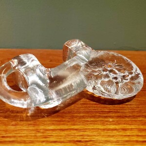 May include: A clear glass paperweight with a floral design. The paperweight is shaped like a flower with a stem and leaves.