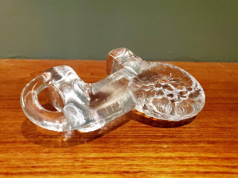 May include: A clear glass paperweight with a floral design. The paperweight is shaped like a flower with a stem and leaves.
