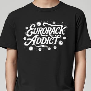 May include: Black t-shirt with the white text "Eurorack Addict" in a stylized font. The design includes white splatters and circular accents, creating a bold graphic. The shirt is a classic crew neck style.