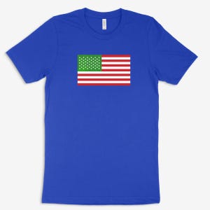 May include: A royal blue short-sleeve t-shirt featuring a rectangular graphic on the chest. The graphic depicts a flag with a green canton containing white stars and horizontal red and white stripes, mimicking the layout of the American flag.