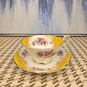 Peut inclure: Un service à thé vintage composé d'une tasse et d'une soucoupe. La tasse et la soucoupe ont une bordure jaune avec un motif floral. La tasse a une anse dorée et un intérieur blanc avec un motif floral. La soucoupe est ronde et présente un motif floral assorti.